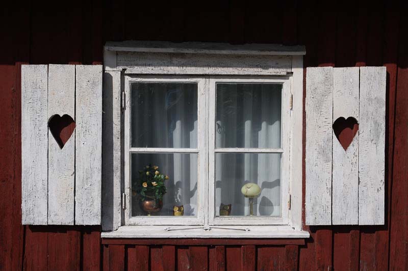 Rött trähus med vita hjärtformade fönsterluckor i Mariestad