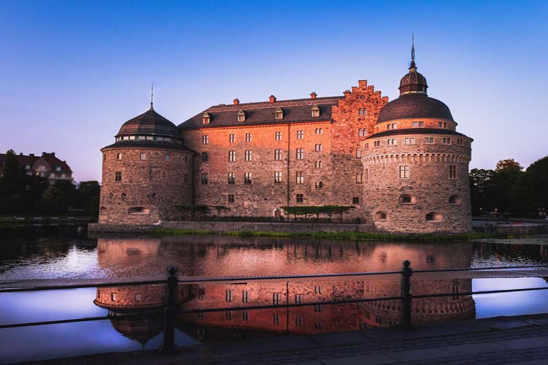 Örebro slott med torn och bro över Svartån i kvällsljus